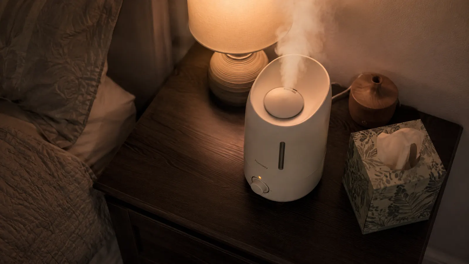 Nightstand flat-lay showing a humidifier with visible mist, a folded tissue box, and a small empty diffuser pushed to the side