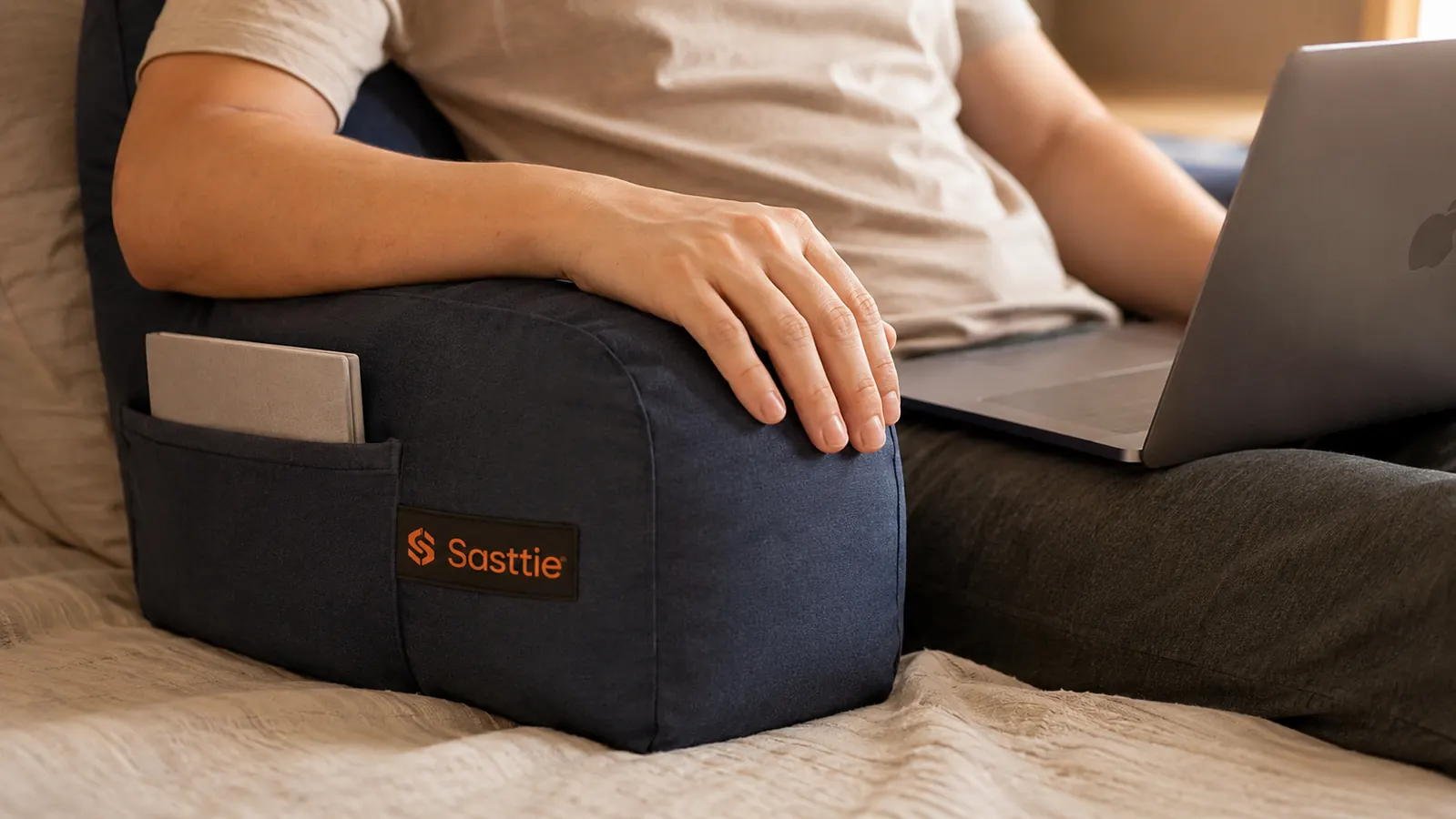 Close-up of hand resting on the armrest of the Sasttie reading pillow while balancing a laptop on the lap